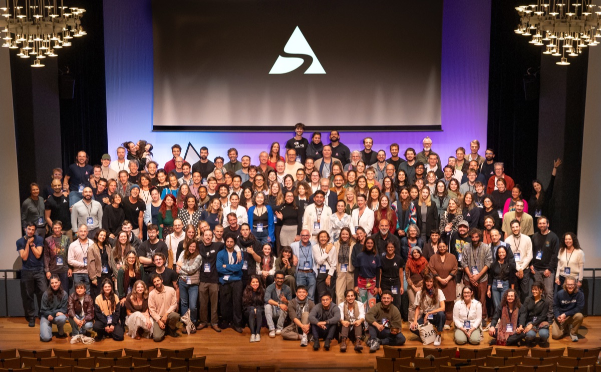 Group photo of speakers, volunteers and attendees on the main stage of the Kultur & Kongresshaus Aarau, the ALPS logo on the screen behind them
